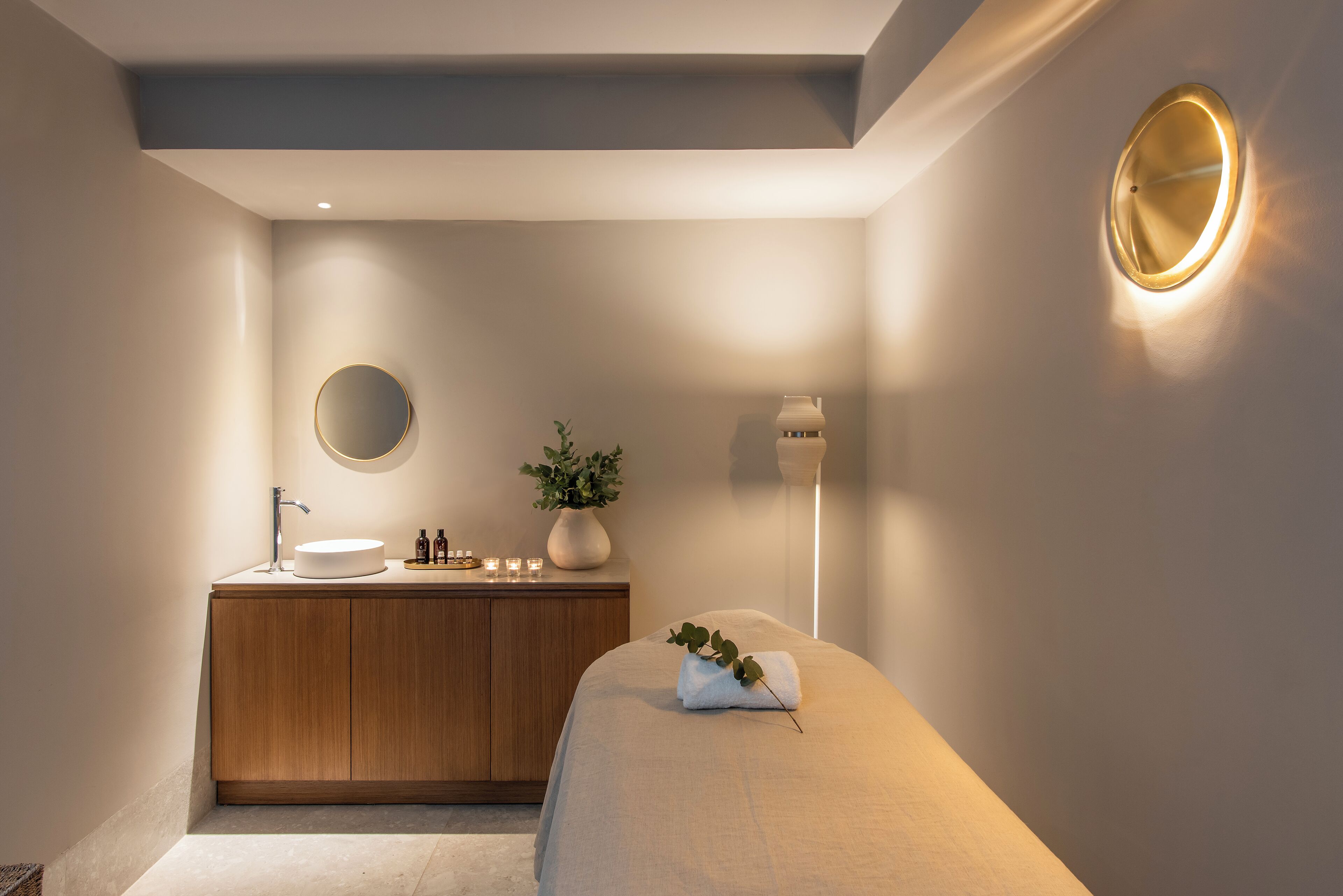 A modern bathroom with a wooden vanity, a round mirror, a potted plant, and a towel on a bench.