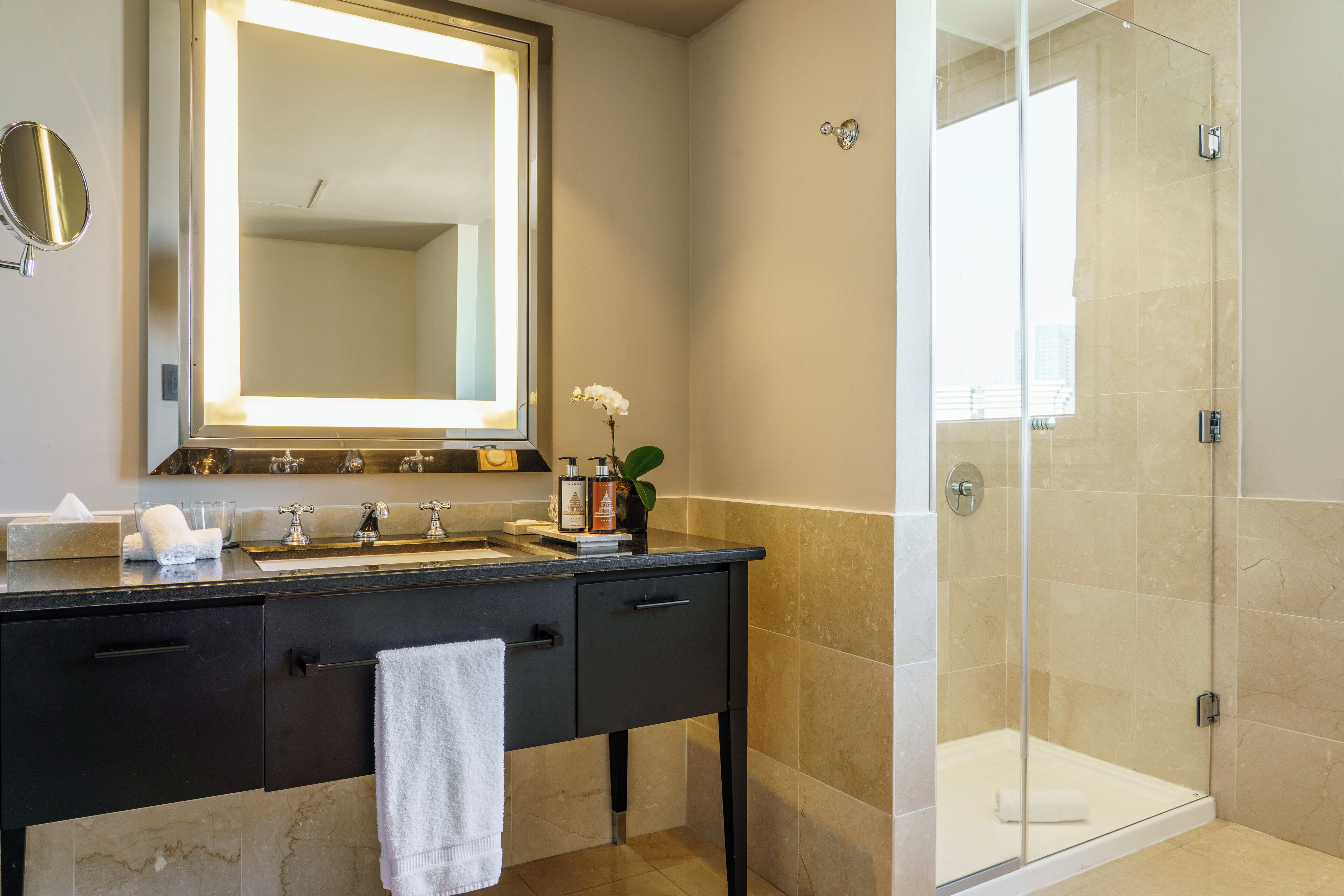 A modern bathroom with a large mirror, a sink, and a glass-enclosed shower.