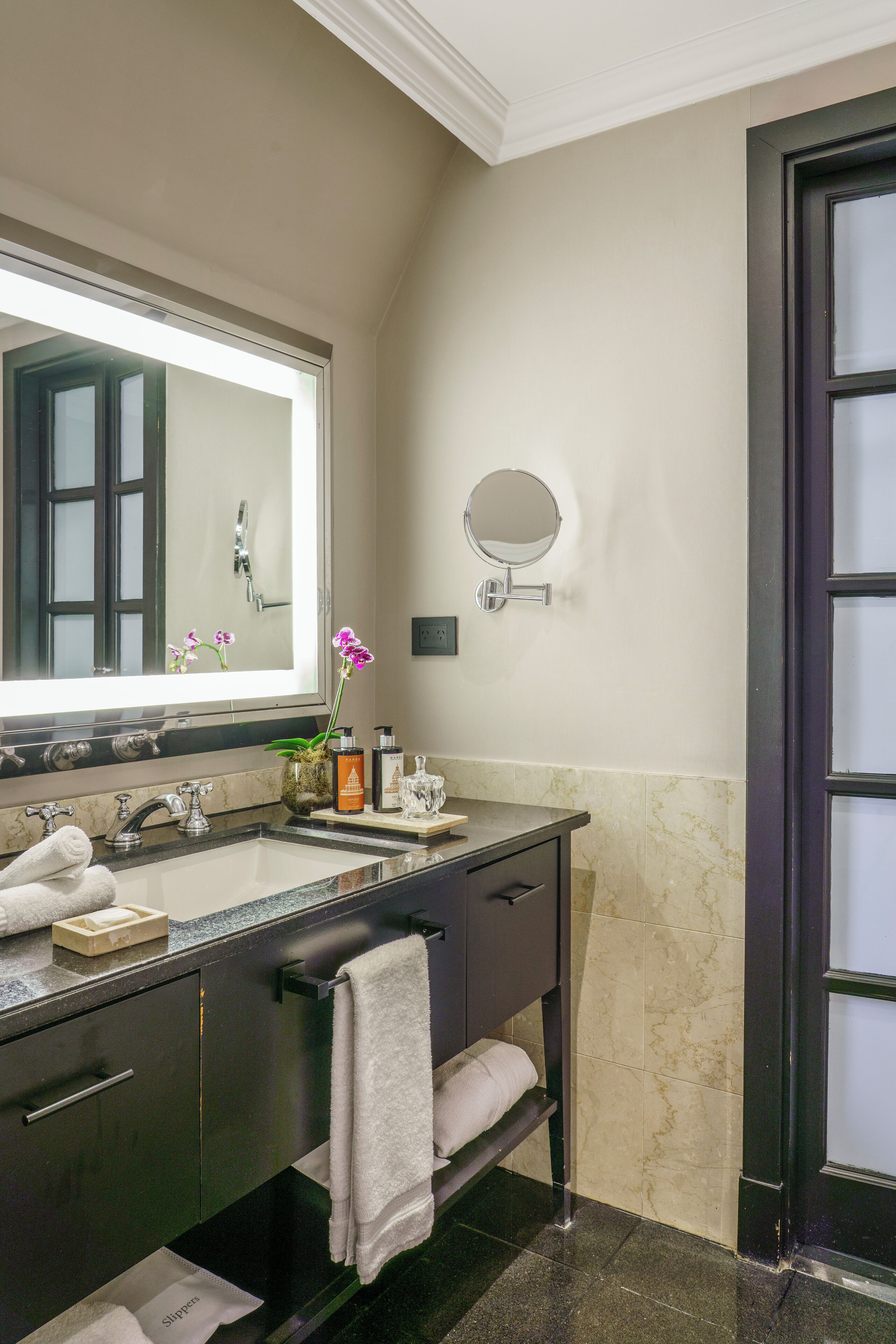 A modern bathroom with a large mirror, two sinks, a towel rack, and a small round mirror on the wall.