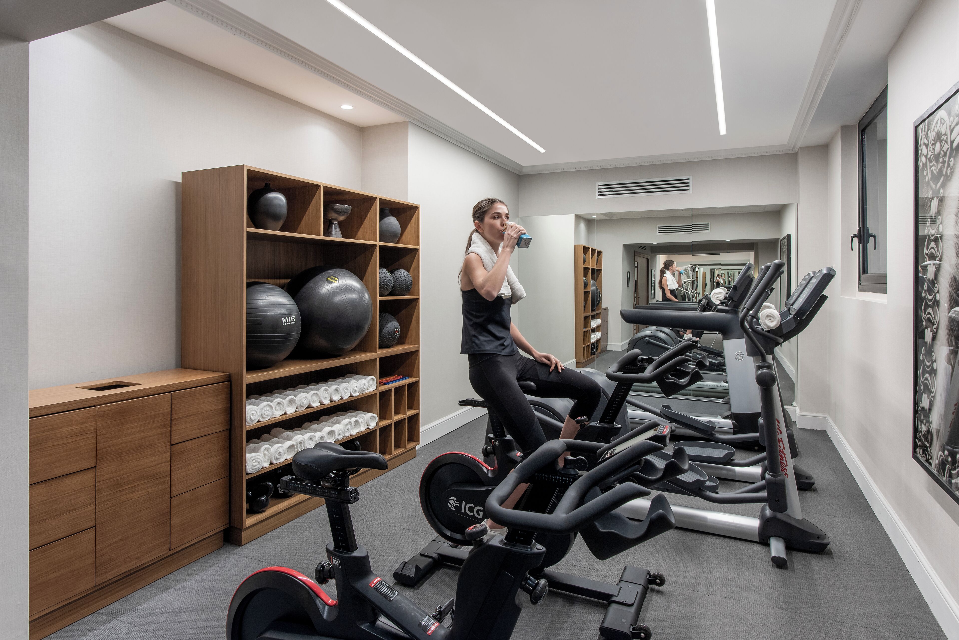 A modern gym with multiple exercise machines, a wooden storage unit with exercise balls, and a mirror wall.