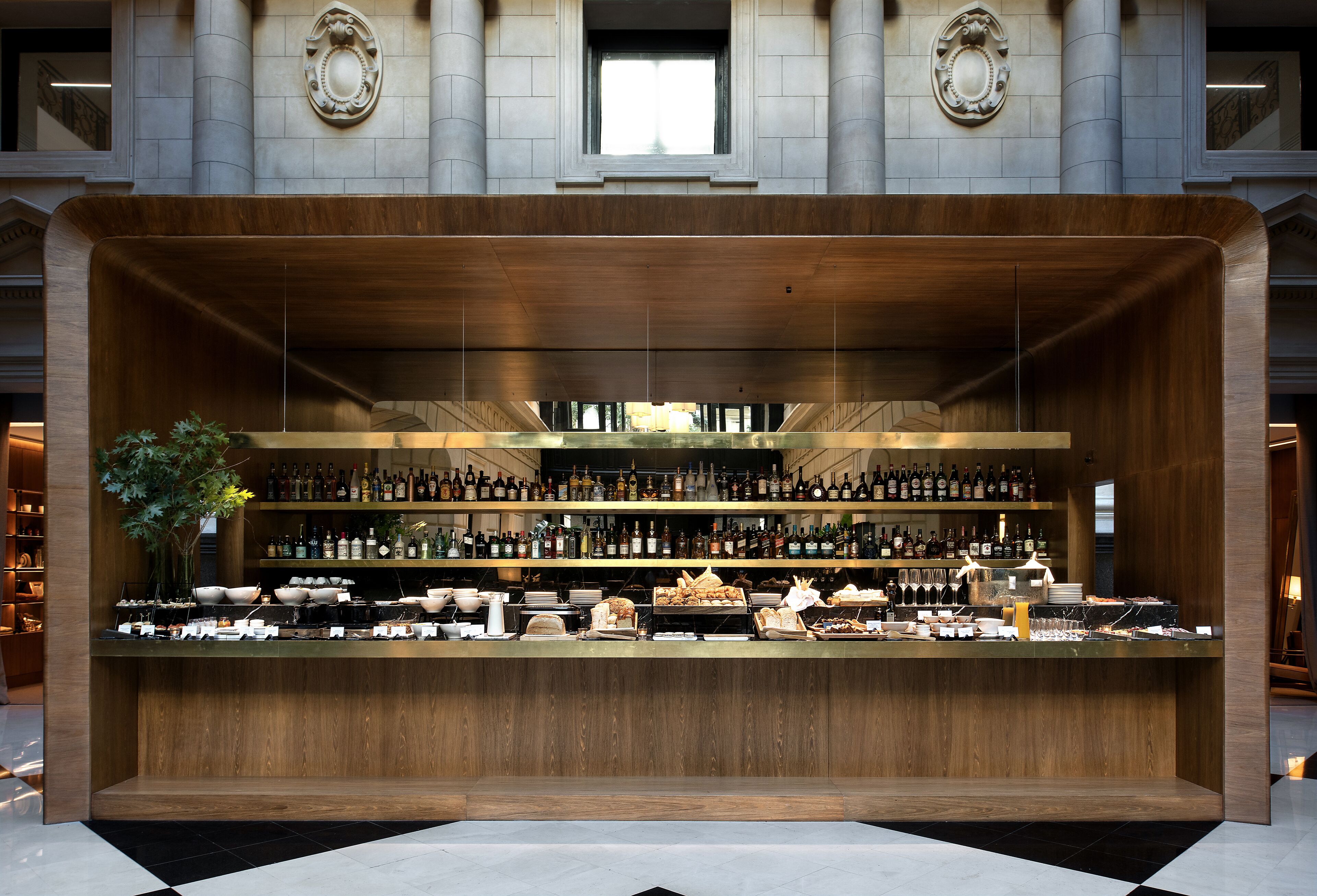 A bar area with a wooden counter, shelves of bottles, and a large window above.