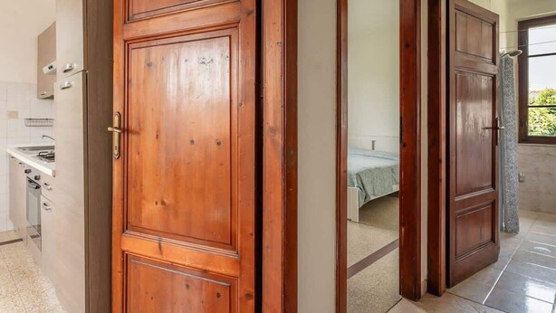 A wooden door leading to a bedroom with a bed and a window.