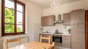 A modern kitchen with wooden cabinets, a stainless steel refrigerator, and a window with a view of greenery.