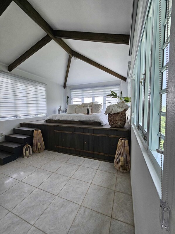 A loft bedroom with a sloped ceiling, built-in wooden bed, large windows, and a staircase leading to an upper level.