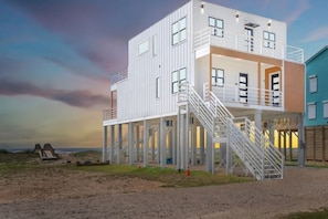 A modern multi-story building with a balcony and a staircase leading to the upper level. - Luxury Beachfront Retreat w Gulf & Wetland Views - Game Room - 4 Decks-Sleeps 16 (Freeport)