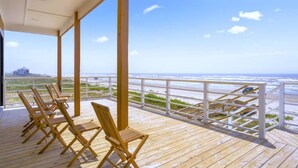 A wooden deck with beach chairs overlooking a beach and ocean.