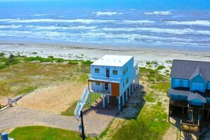 Una propiedad costera con un edificio principal y una estructura secundaria, ambas elevadas sobre pilotes, con vistas a la playa y al océano.
