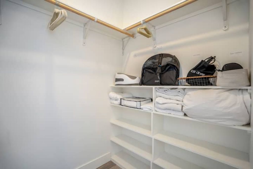 Um armário branco com prateleiras, um porta-sapatos suspenso e roupas dobradas com cuidado.
