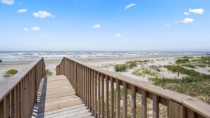 A wooden boardwalk leading to a beach with sand dunes and the ocean in the background.