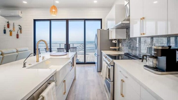 A modern kitchen with white cabinetry, a large window, and a view of the ocean.