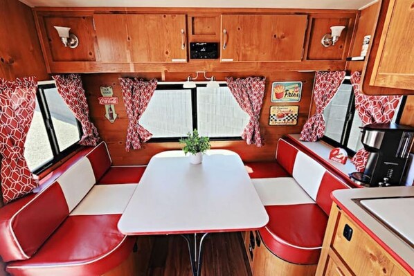 A compact RV interior with a dining area, red and white seating, a small table, and a kitchen area with a microwave.