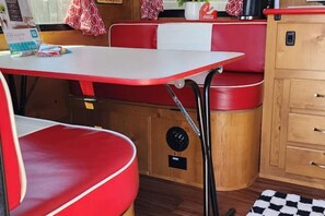 A compact kitchenette with red and white furnishings, a small table, and a cabinet with drawers.