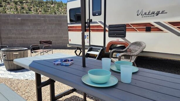 Um camping com mesa para piquenique, cadeiras e um trailer antigo.