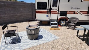 Relax in a serene outdoor space with a vintage RV in the background, surrounded by a mat, chair, and wooden table.