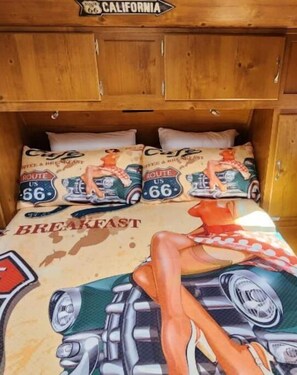 A bed with a Route 66-themed bedspread and pillows, wooden headboard, and a sign above indicating California.