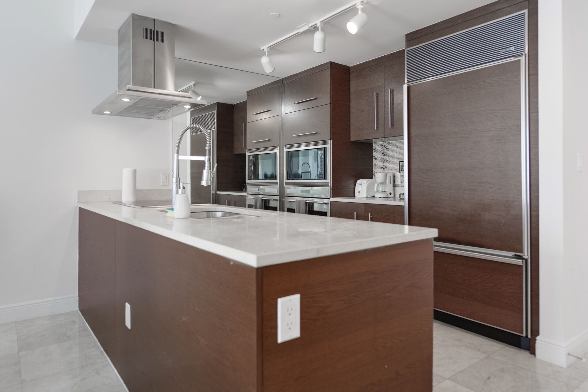 A modern kitchen with a central island, stainless steel appliances, and a dark wood finish.