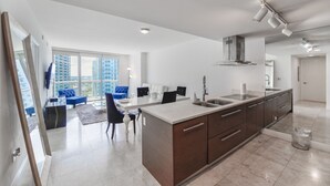 A modern apartment with a kitchen, dining area, and a large window overlooking a cityscape. - Icon Tower 3 (Miami)