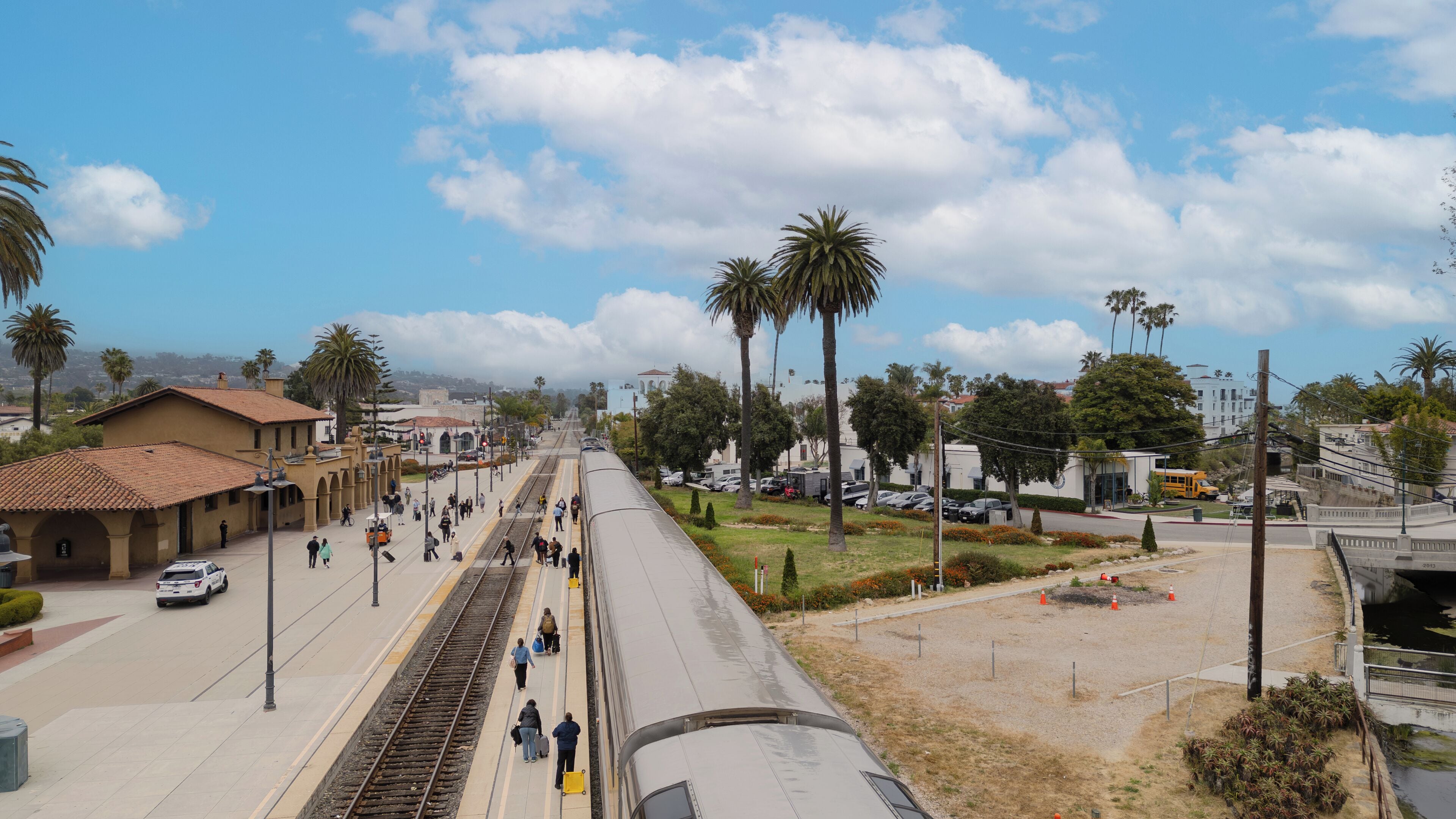 Un quai de gare avec un train, des passagers et des palmiers.