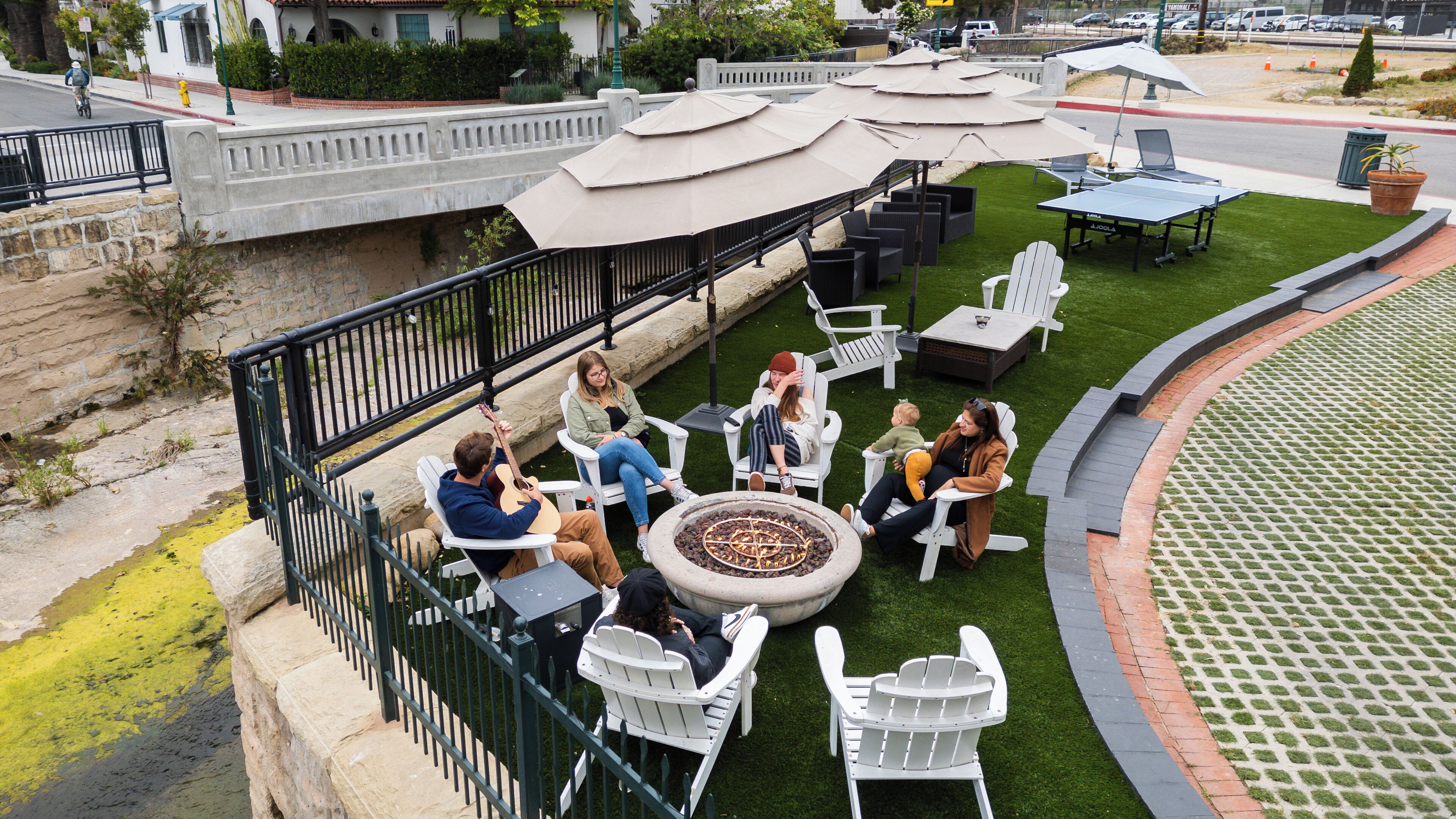 Un espace extérieur aménagé avec des chaises et des tables blanches, un foyer et des parasols.