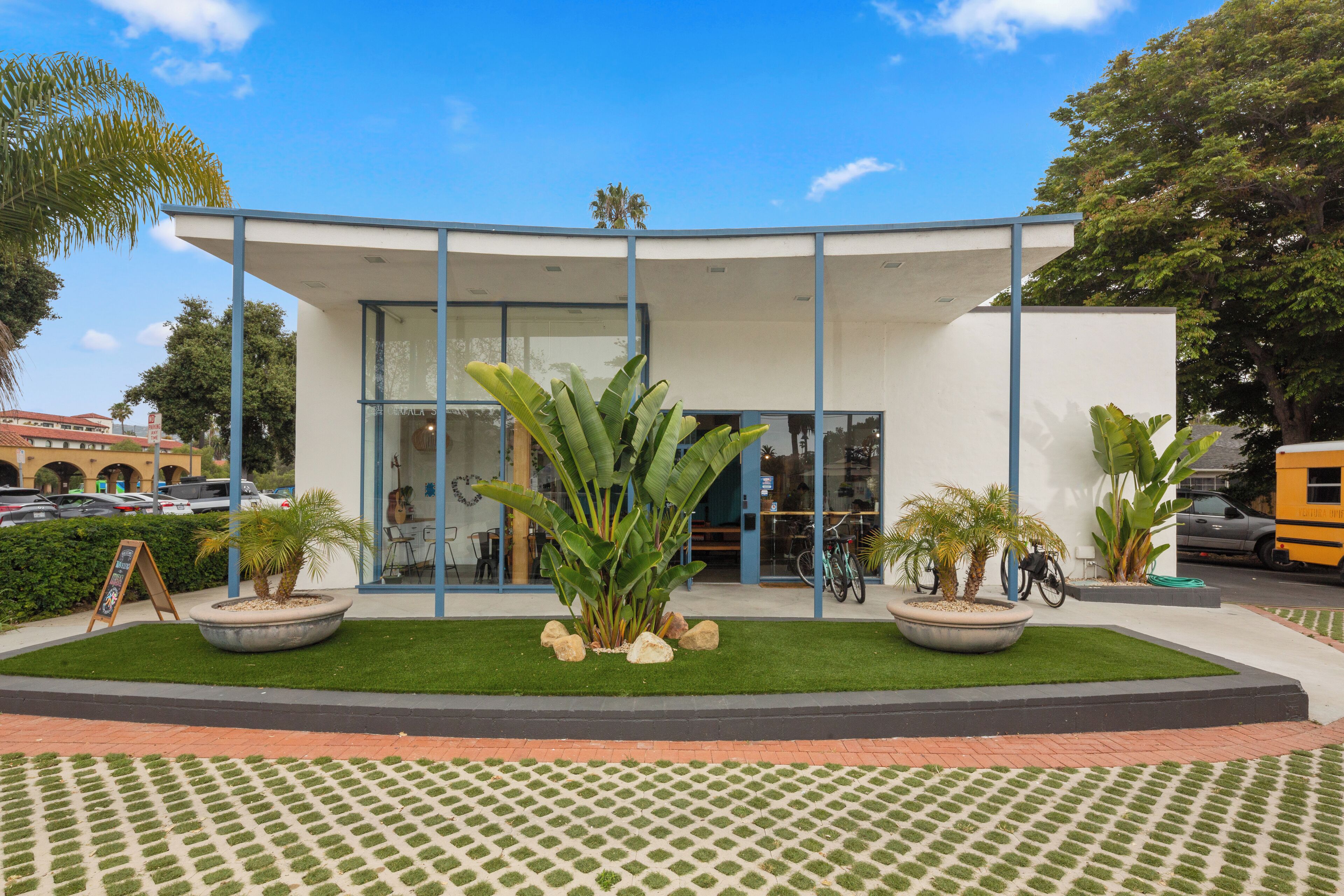 A modern building with a glass facade, surrounded by a landscaped garden with palm trees and a paved walkway.