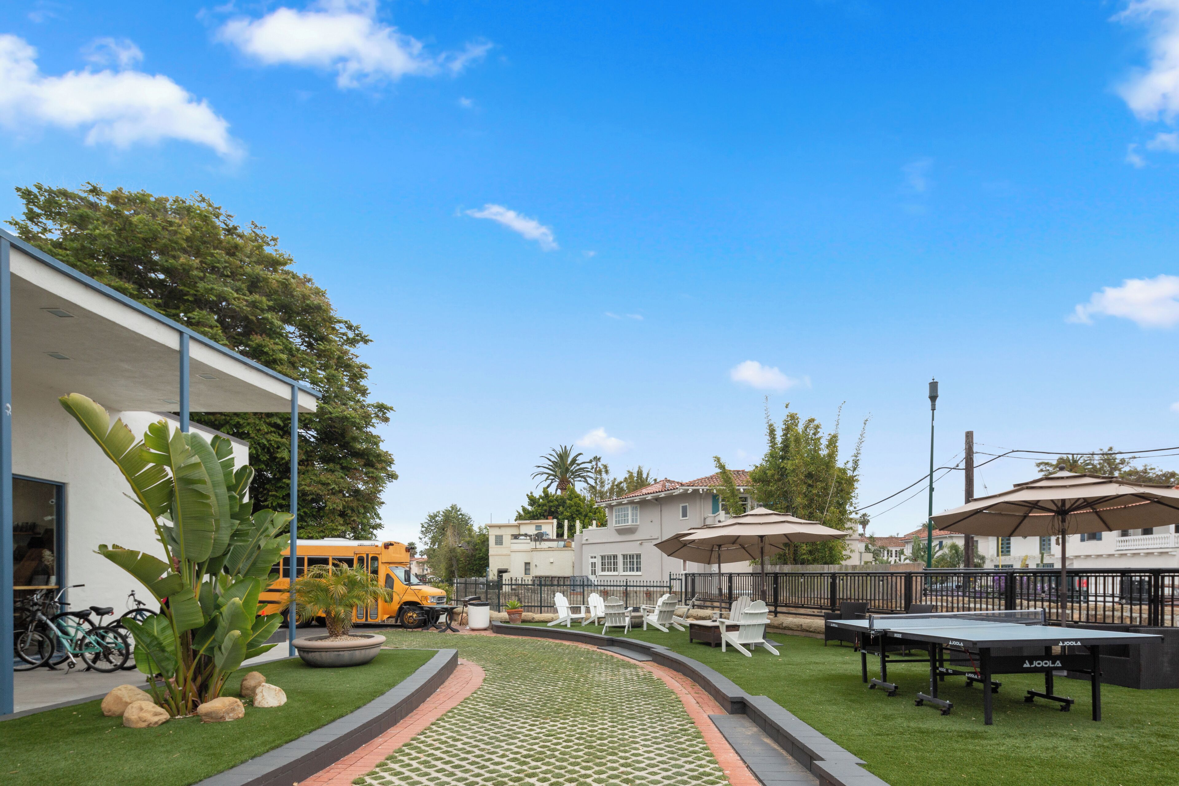 A courtyard with a green lawn, outdoor seating, and a bus in the background.