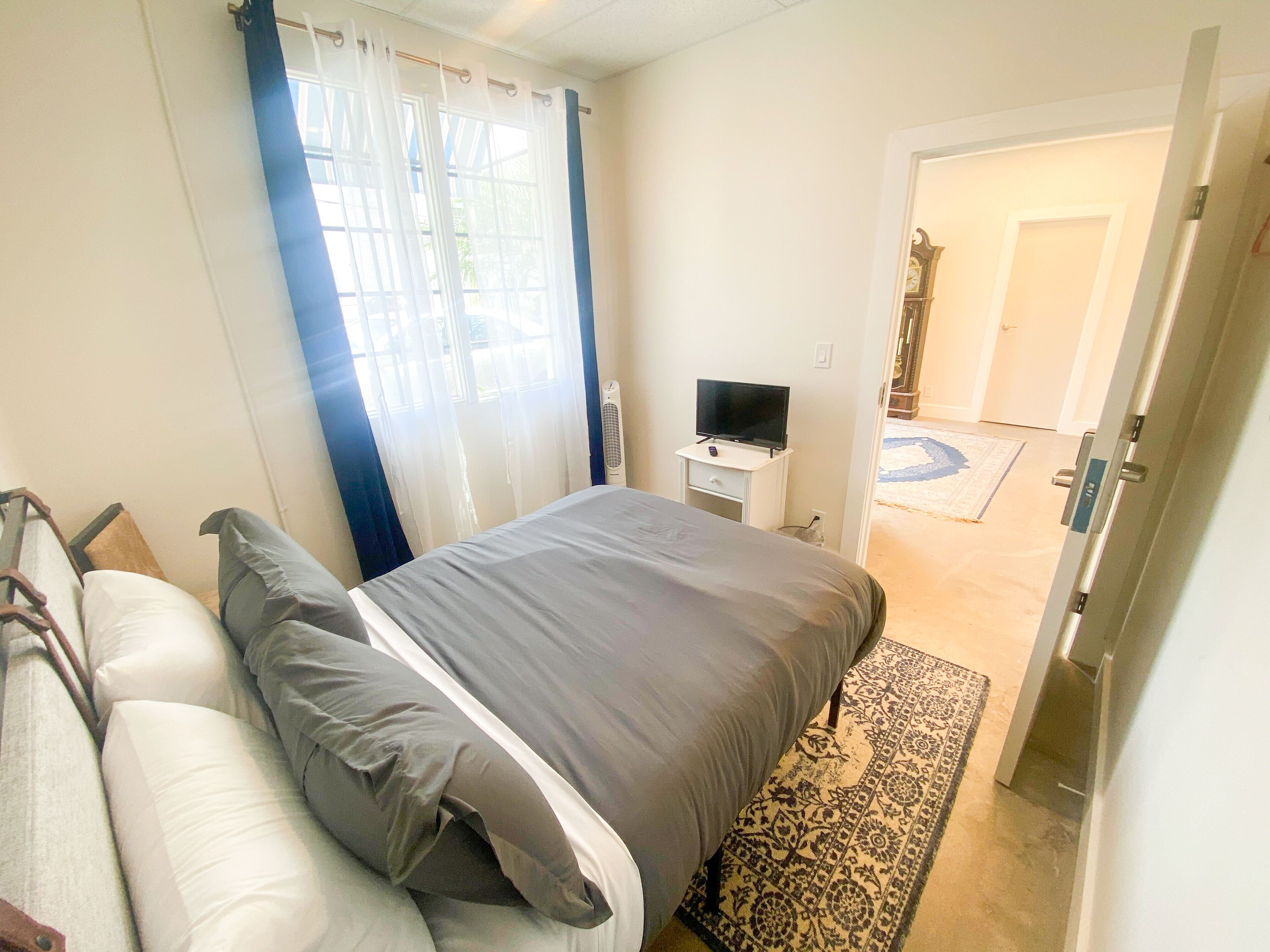 A bedroom with a bed, a TV on a small table, and a view of a hallway.