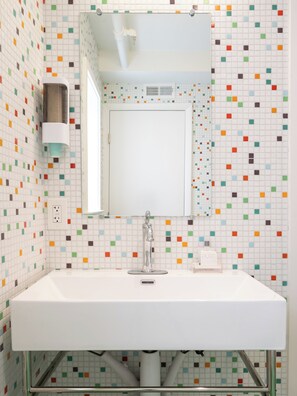 A bathroom with a white sink, a mirror, and colorful mosaic tiles on the walls.