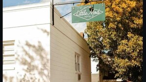 Ein weißes Gebäude mit einem Schild für 'Little Mod Hotel' und einer Terrasse mit Außenbestuhlung.