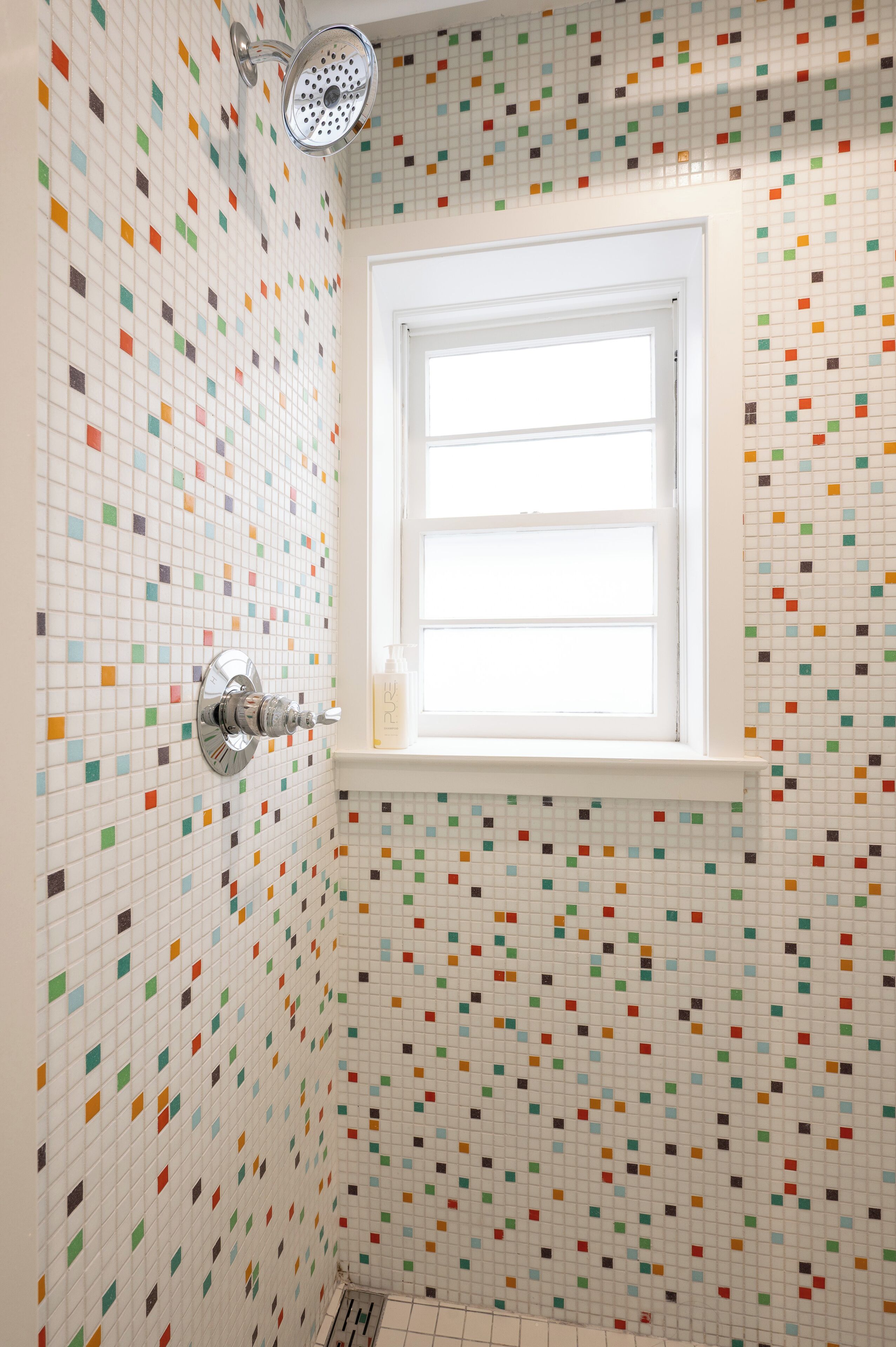 A bathroom with a colorful mosaic tile wall, a showerhead, and a window.