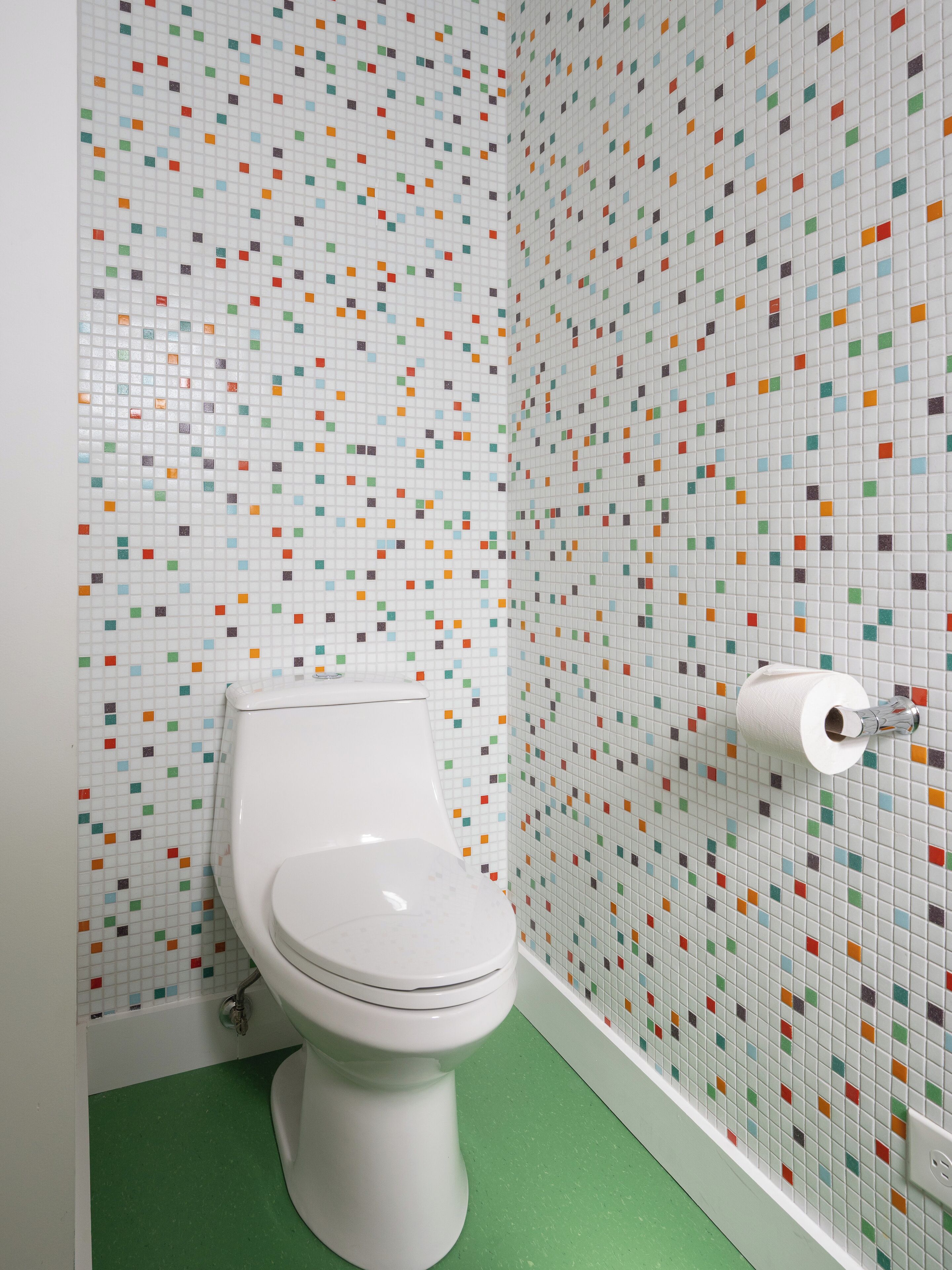 Ein Badezimmer mit Toilette, grünem Boden und einer Wand mit farbenfrohen Mosaikfliesen.
