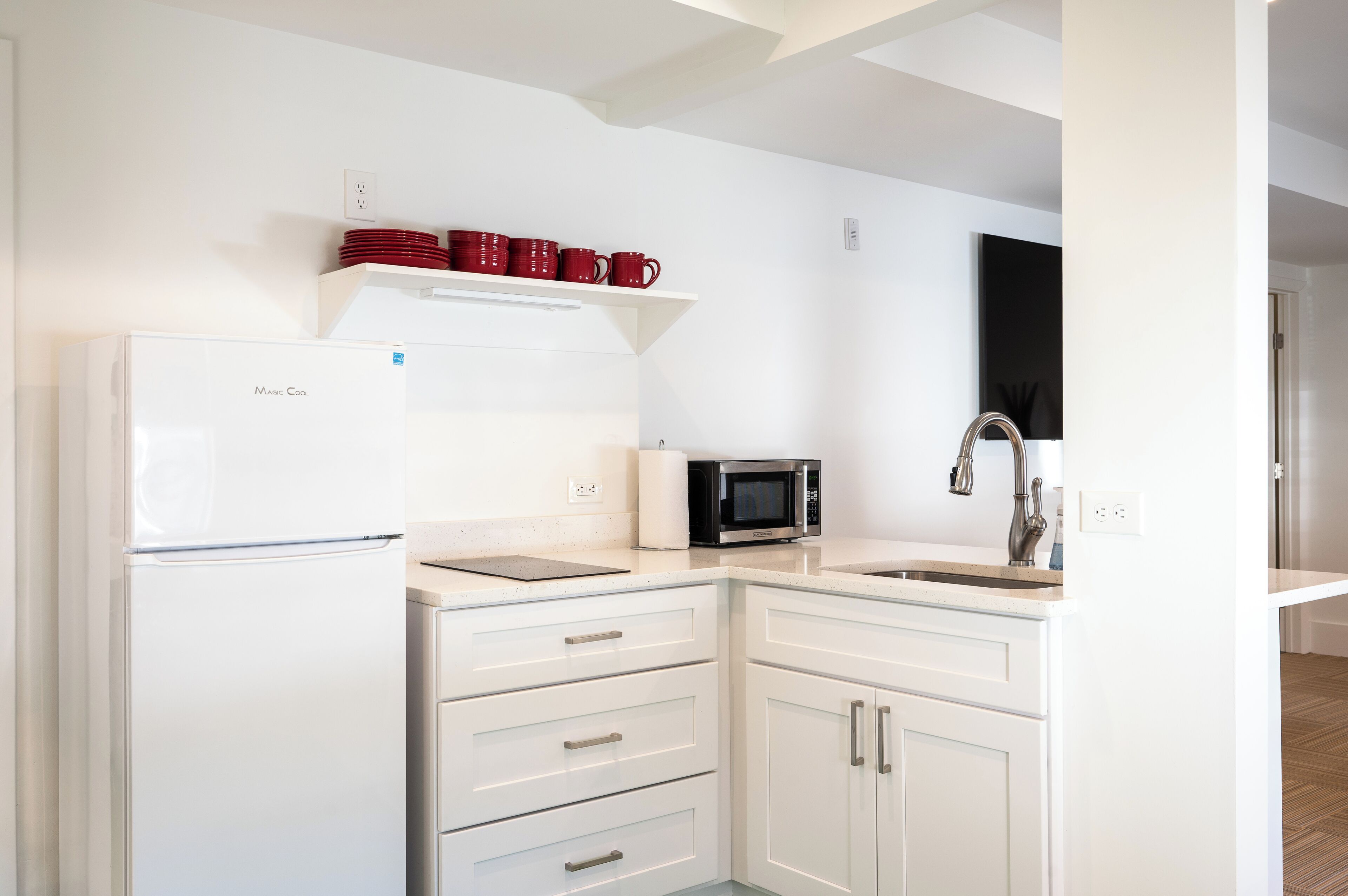 A modern kitchen with white cabinets, a white refrigerator, a microwave, and a sink.