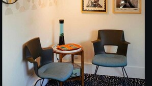 Ein Zimmer mit zwei Stühlen, einem kleinen Tisch, einer Wandklimaanlage und zwei gerahmten Bildern.