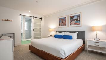 Une chambre d’hôtel moderne dotée d’un grand lit, de deux tables de chevet avec lampes, d’une armoire et d’une porte coulissante en verre donnant sur la salle de bain.