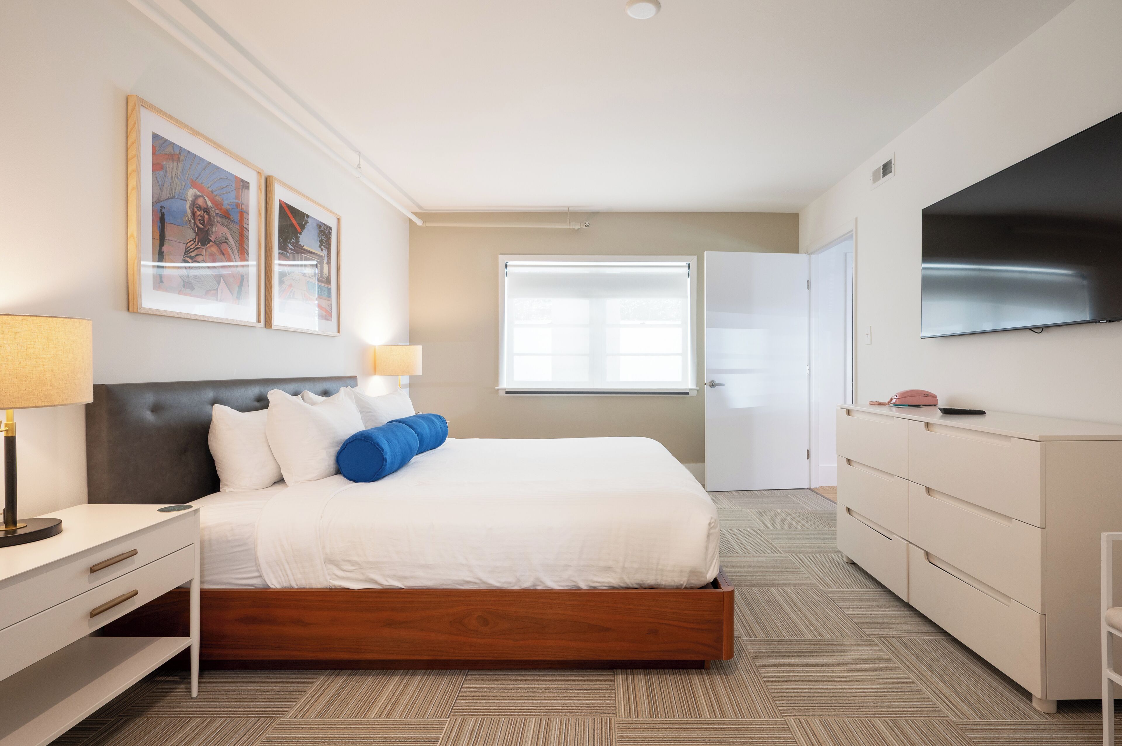 A modern hotel room with a large bed, bedside tables, a TV, and artwork on the wall.
