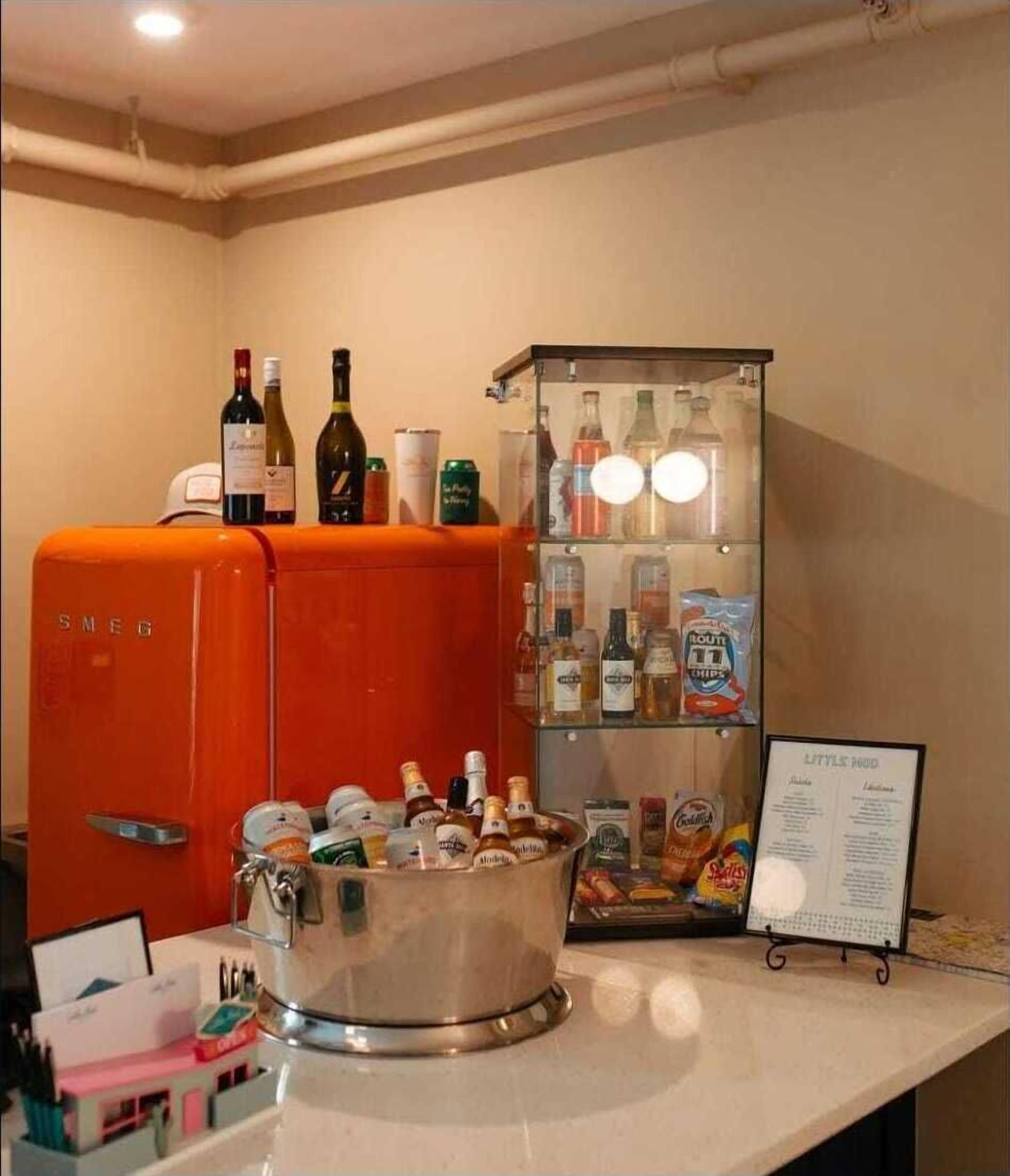 A minibar with a variety of beverages and snacks, an orange refrigerator, and a menu stand.