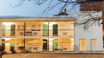 Un edificio de dos pisos con balcones, mobiliario exterior con sombrillas y un pequeño jardín.