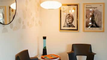 Een kamer met twee stoelen, een tafeltje, een wandairconditioner en twee ingelijste foto's.