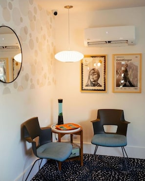 A room with two chairs, a small table, a wall-mounted air conditioner, and two framed pictures.