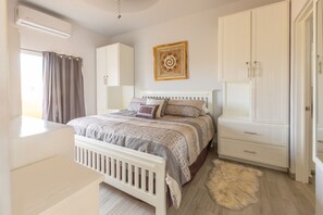 Un dormitorio con cama, armario, radiador y ventana con cortinas.
