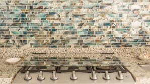 A kitchen with a gas stove, granite countertop, and a backsplash with blue and white tiles.