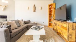 A modern living room with a sectional sofa, a white coffee table, a flat-screen TV, and a wooden cabinet with shelves.