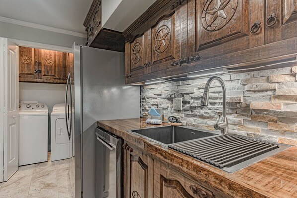 A kitchen with wooden cabinets, a stone backsplash, and a stainless steel sink.