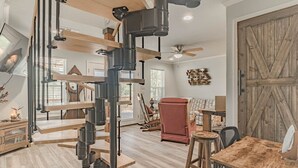 Un vaste espace de vie comprenant une table à manger en bois, un fauteuil rouge et un ventilateur de plafond.
