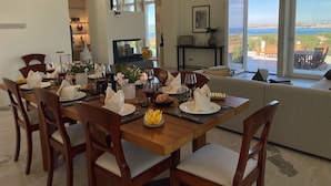 A dining area with a wooden table set for a meal, a sofa, and a view of the outdoors. - Villa OLEANDRA: Luxe, daily service, sea & sunset impressive views, 24mt pool (Isola)