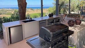 An outdoor kitchen with a view of the sea, a wooden table, and chairs. - Villa OLEANDRA: Luxe, daily service, sea & sunset impressive views, 24mt pool (Isola)