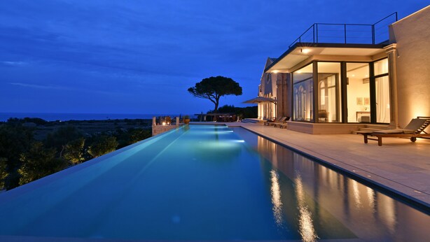 A modern infinity pool with a clear view of the ocean, a large tree, and a contemporary building with a balcony. - Villa OLEANDRA: Luxe, daily service, sea & sunset impressive views, 24mt pool (Isola)