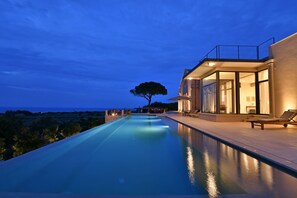 A modern infinity pool with a clear view of the ocean, a large tree, and a contemporary building with a balcony. - Villa OLEANDRA: Luxe, daily service, sea & sunset impressive views, 24mt  pool (Isola)