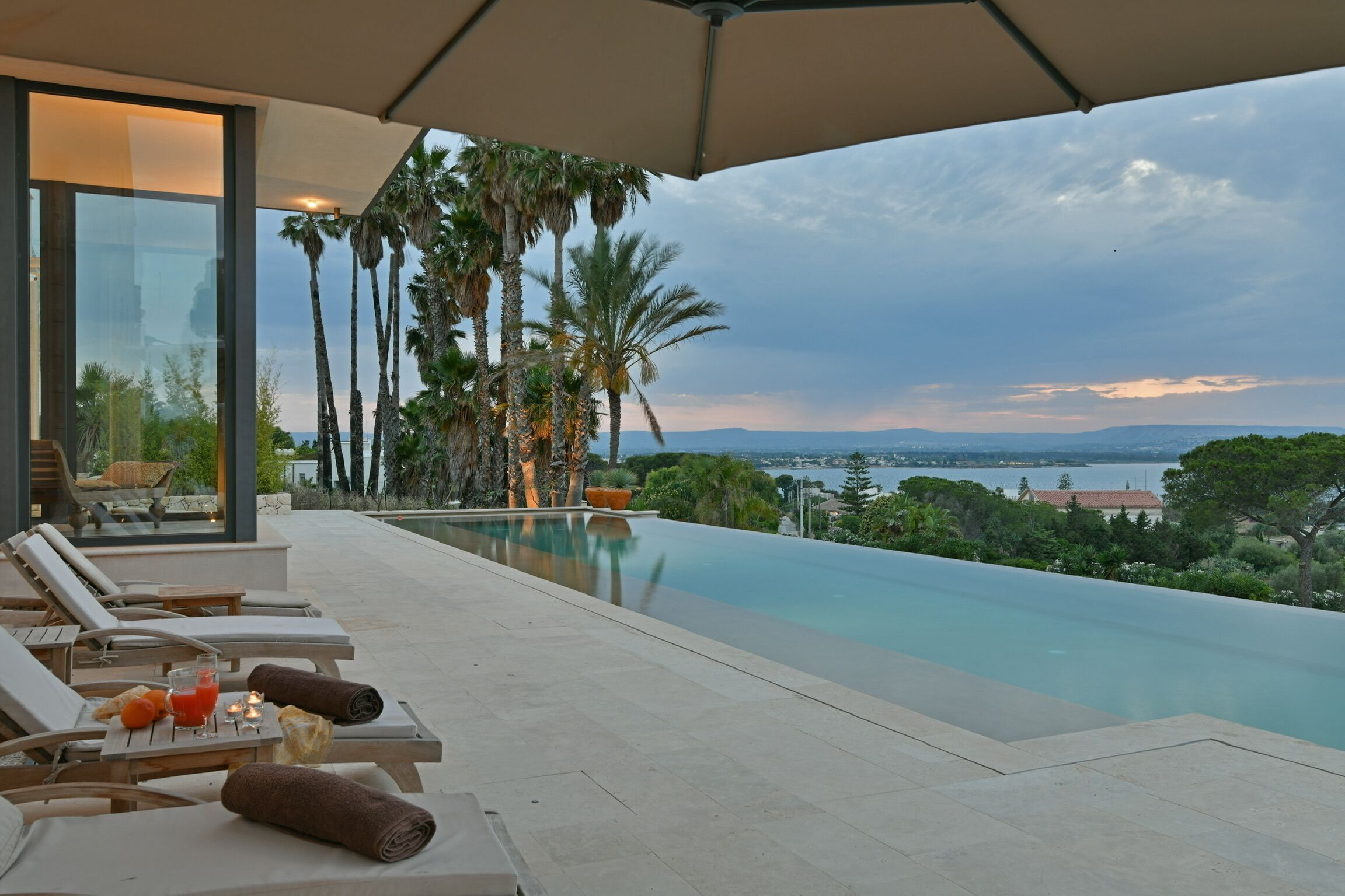 Un espace piscine extérieur moderne, doté de chaises longues et offrant une vue sur la mer.