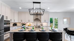 A modern kitchen with a central island, bar stools, and a dining area. - Elysian Shores W/heated Pool & Optional Boat Rental (Mooresville)