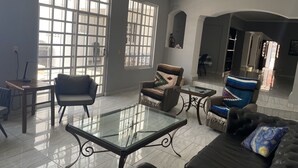 Amplia sala de estar con una mesa de centro de vidrio, sofá de cuero y sillones. Amplias ventanas permiten que la luz natural inunde la habitación.